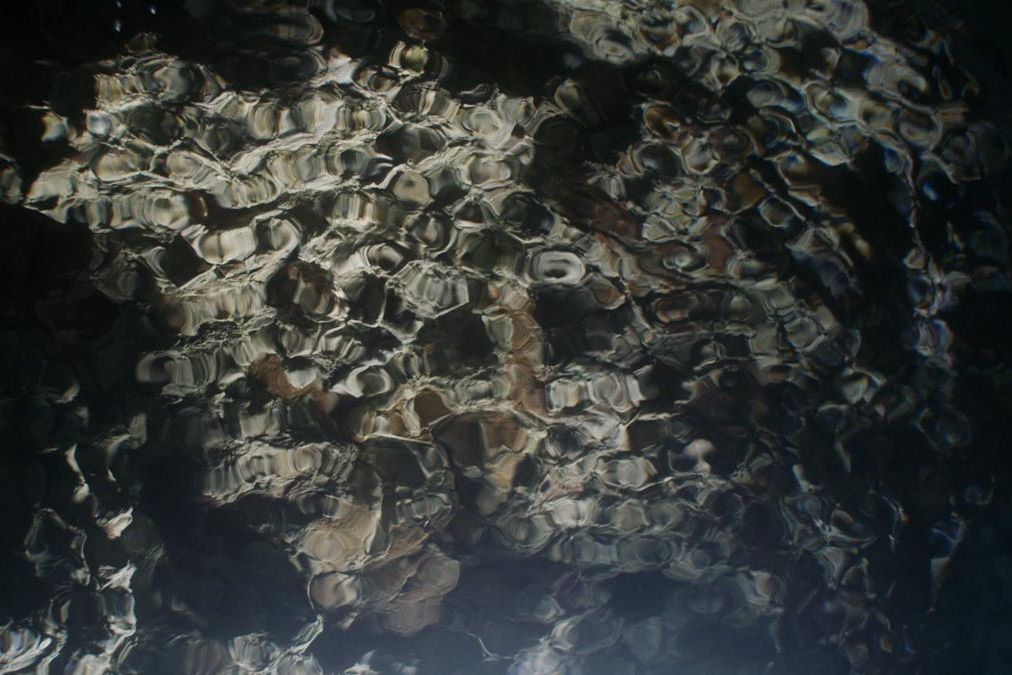 Aufnahme einer Steinformation unter Wasser, die aufgrund der Oberflächenbewegung zu faszinierenden Strukturen verzerrt wird.